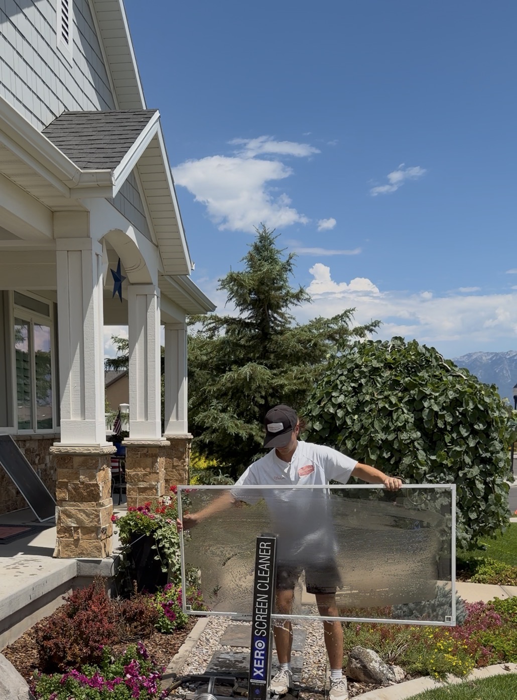 White Collar Windows technician washing a large window screen outside a home